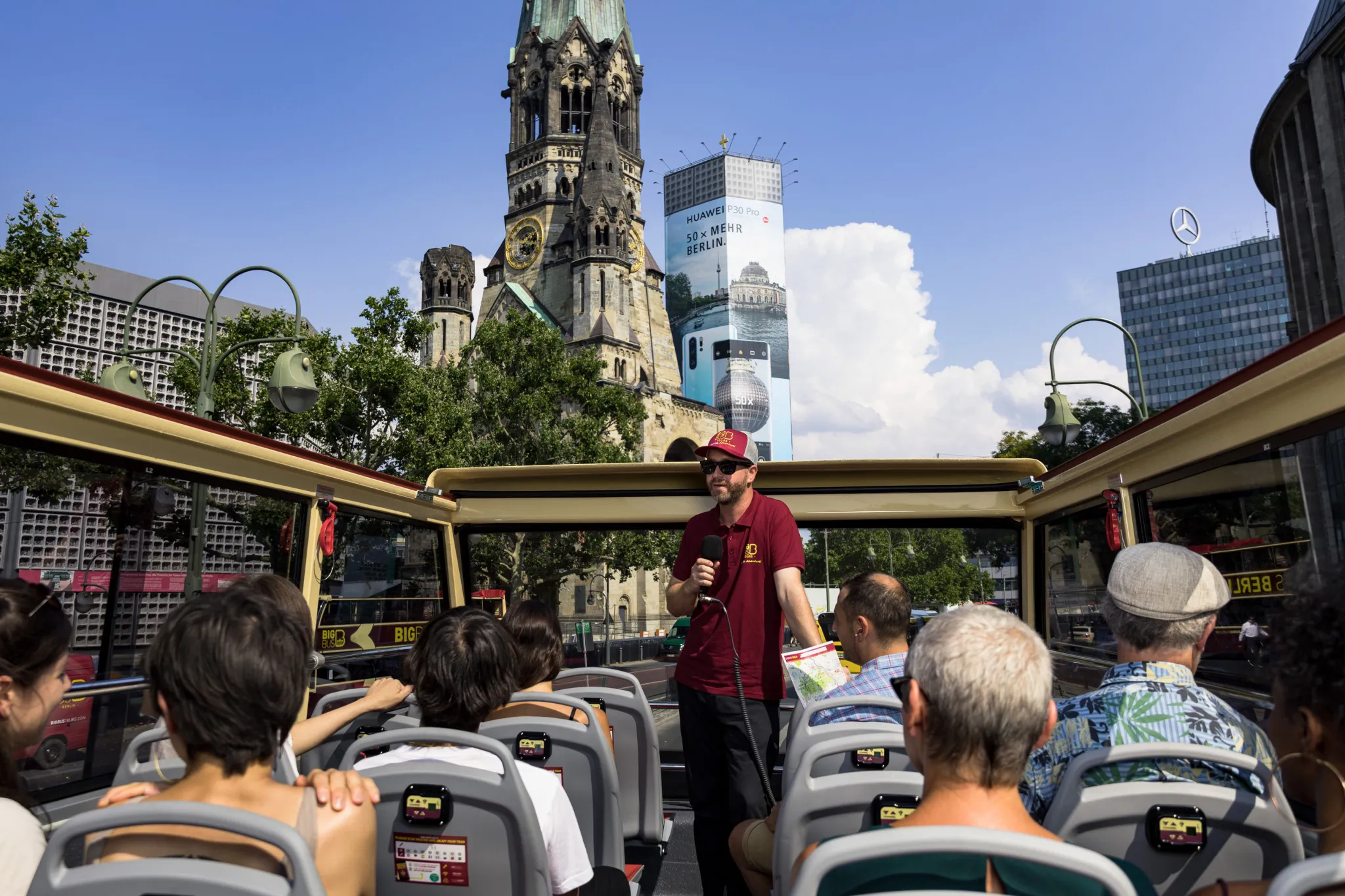 Tourists taking photos from the open roof of a sightseeing bus