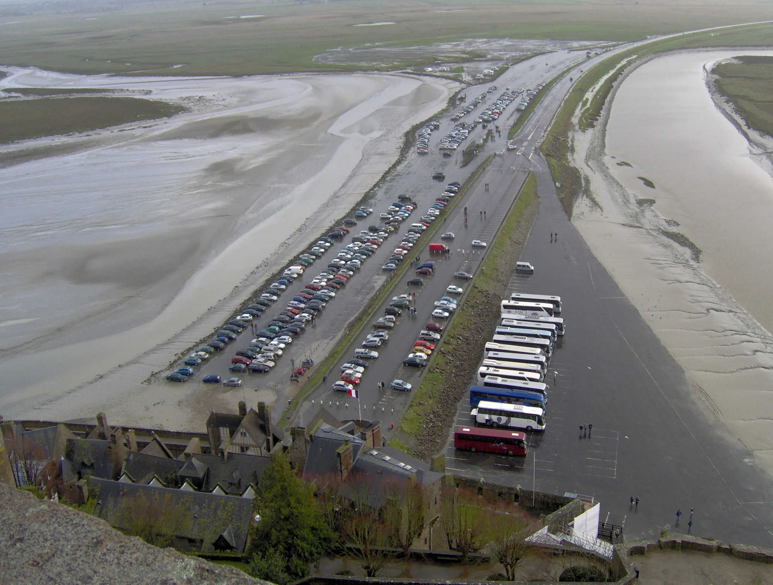 Approach view of Mont-Saint-Michel abbey rising above the village with visitors walking the causeway