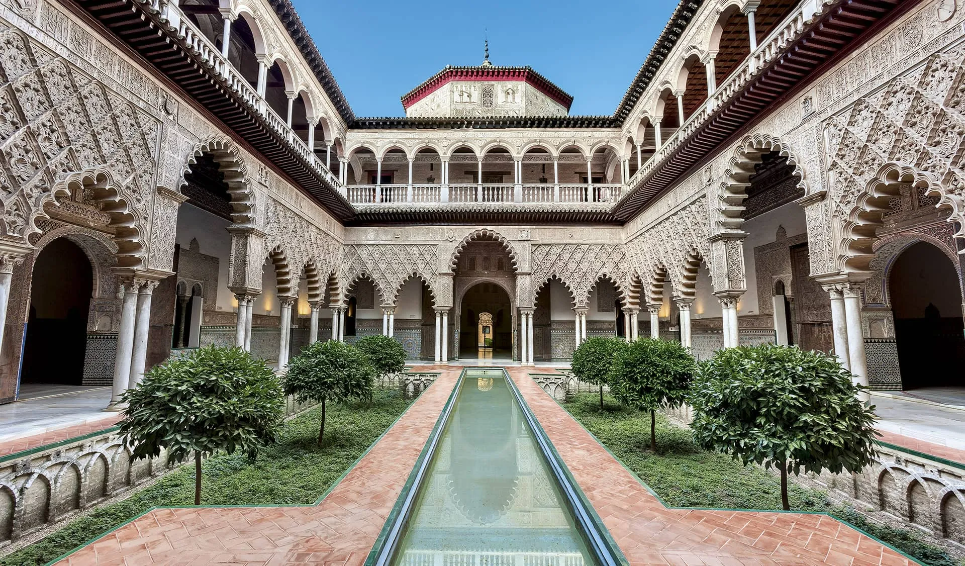 Patio de las Doncellas reflecting pool flanked by ornate Mudéjar arches